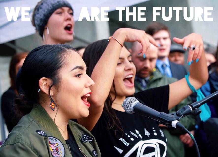 Mia Eastman, a young woman from USA who is a leader with environment group, Earth Guardians, at a rally with other young people, for climate action. Picture also has a caption on top that says 'we are the future', emphasizing on how the reality of climate change is pressing issue for the children of today.