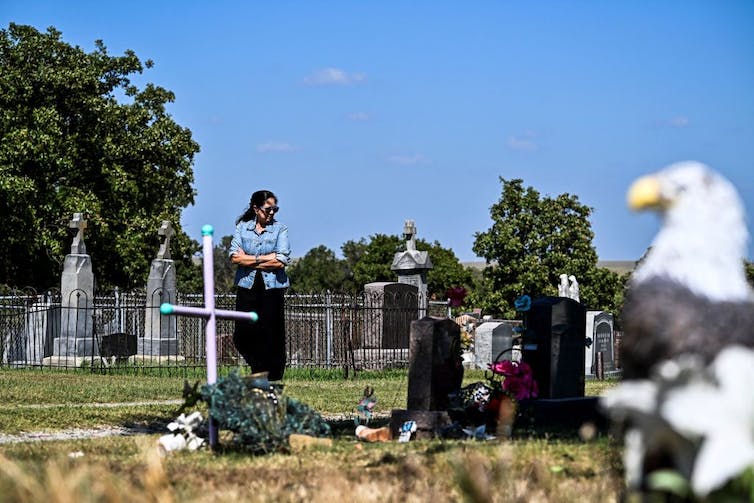 A woman wearing a jean jacket and sunglasses gazes at gravestones.